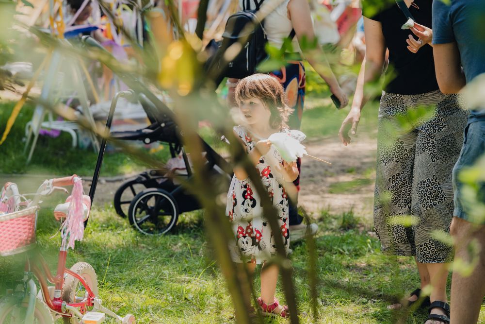 w plenerze, dziecko za drzewem, w oddali inne osoby niewyraźne