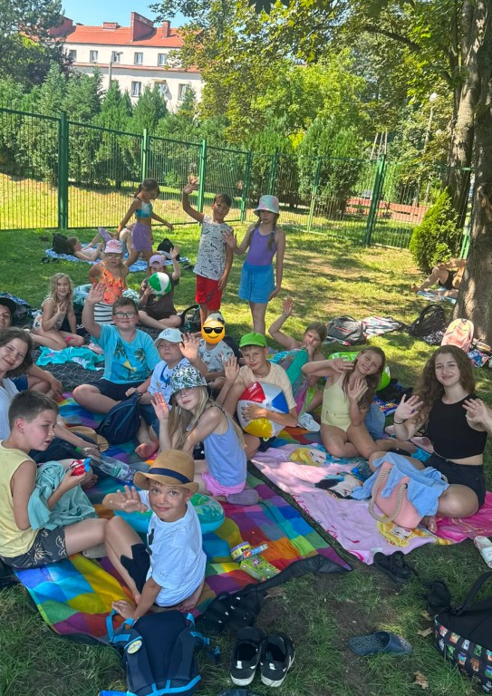 Zdjęcie grupowe, dzieci siedzą na kocu i patrzą w kierunku osoby robiącej zdjęcia.