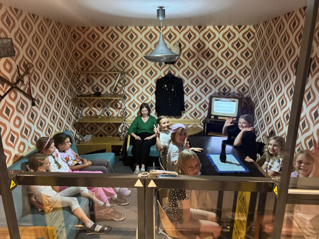 Grupa dzieci w retro pokoju, jest z nimi dorosła osoba.