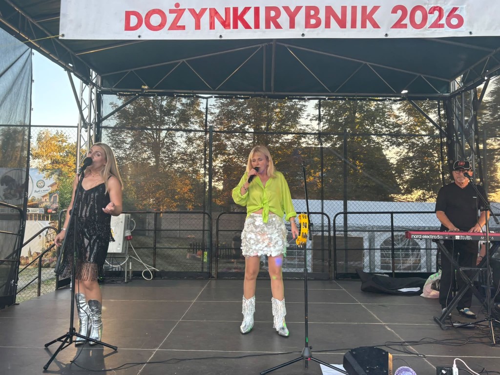 sytuacja sceniczna, scena plenerowa, pod dachem sceny fragment banneru dożynki Rybnik 2026. Na scenie dwie kobiety śpiewają do mikrofonów, przy instrumencie klawiszowym mężczyzna.