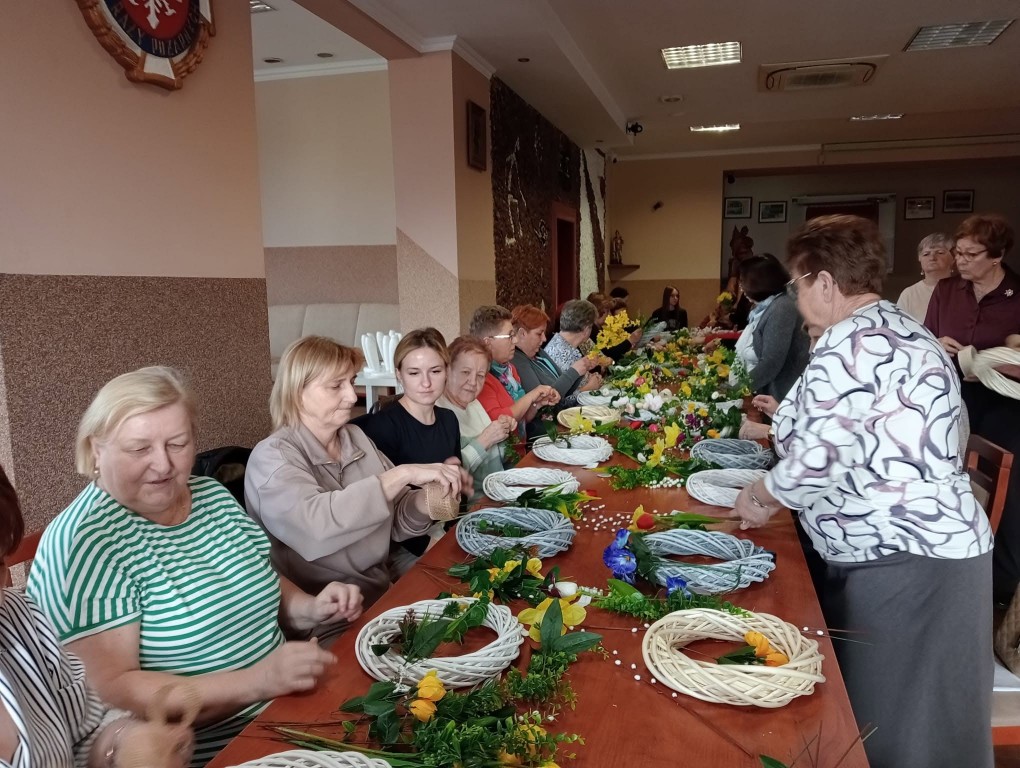 grupa kobiet przy długim stole przygotowuje wianki