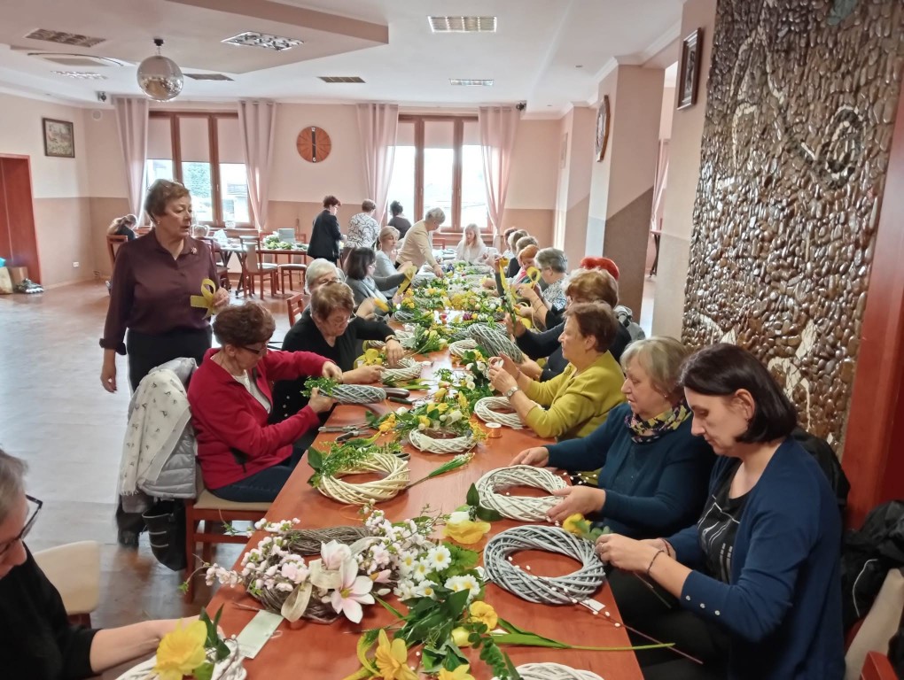 grupa kobiet siedzi przy stołach podczas warsztatu, przygotowują wianki