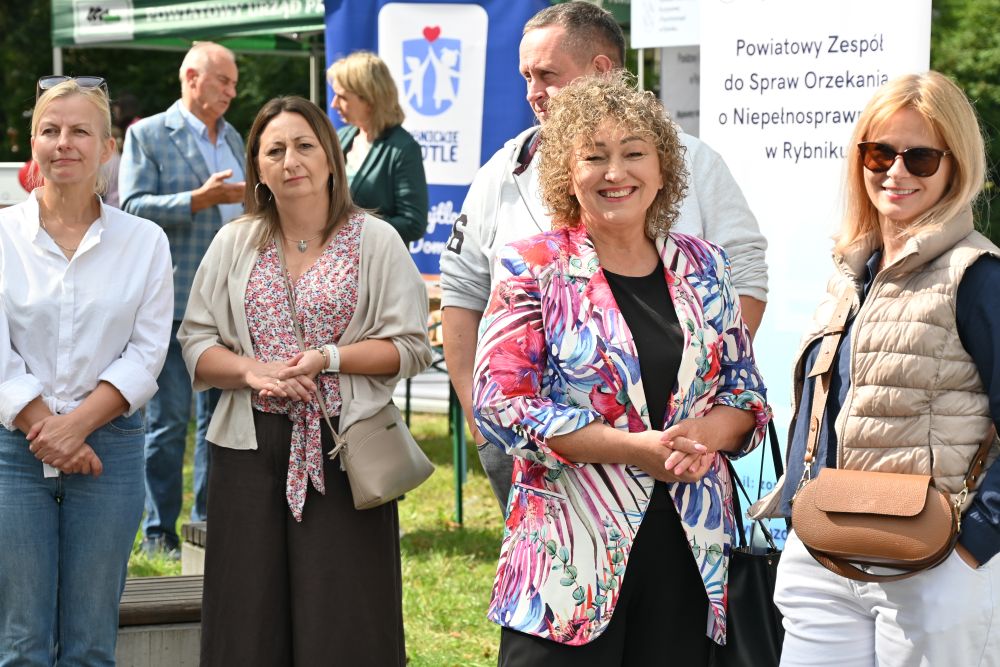 Plener, grupa osób stoi i spogląda w stronę fotografa, w tle banery reklamowe.