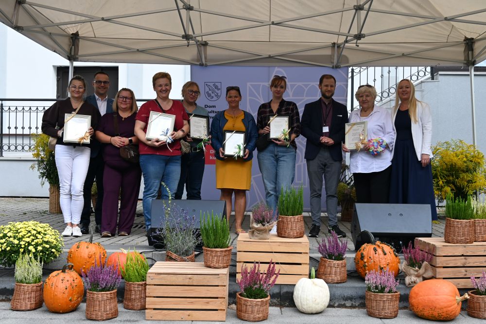 Plener, grupa osób, trzyma z przed sobą obrazki, pozują do zdjęcia. Sytuacja sceniczna.
