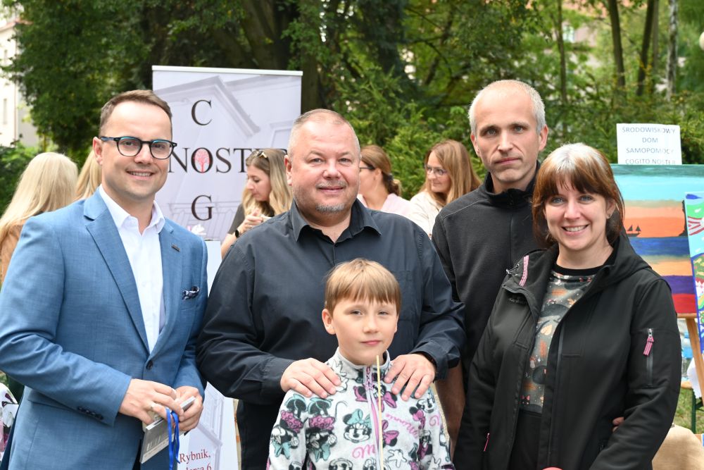 Grupa 5 osób pozuje  do zdjęcia, na pierwszym planie dziecko. W tle widać drzewa.