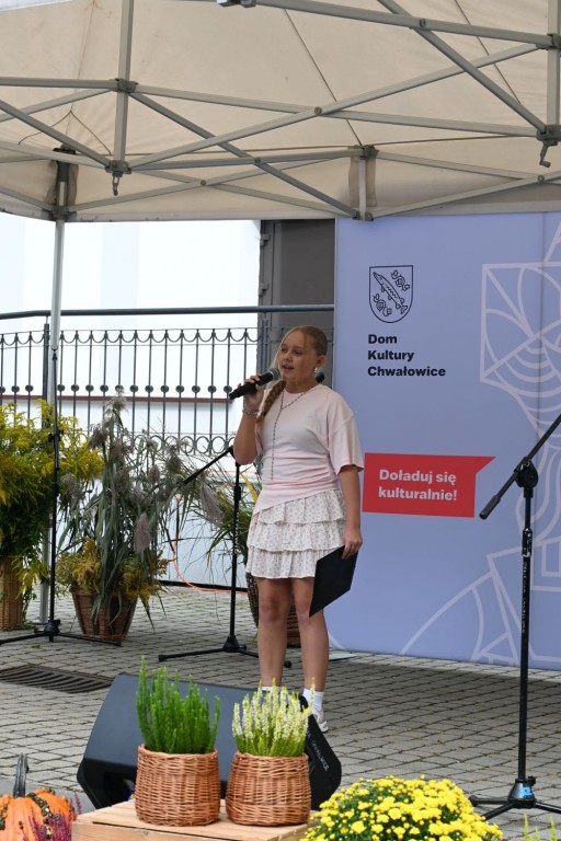 Młoda dziewczyna śpiewa do mikrofonu, w jednej ręce trzyma mikrofon w drugiej podkładkę.