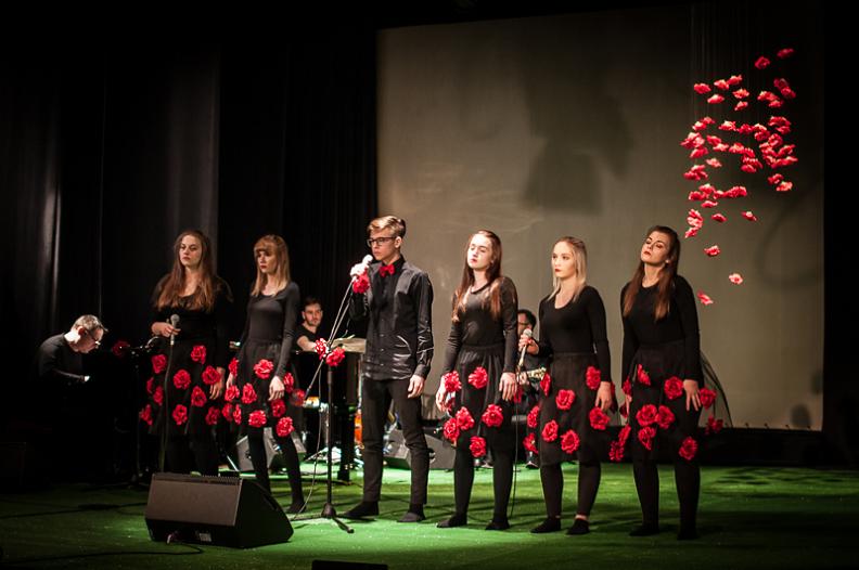artyści na scenie, pięć kobiet z sukienkami w róże i mężczyzna przy mikrofonie