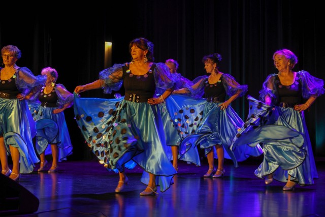 seniorki tańczą na scenie mają czarno niebieski sukienki w kropki z bufiastymi rękawami są podświetlone różowym światłem.