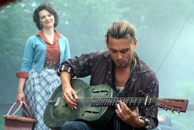 na pierwszym planie mężczyzna gra na gitarze, za nim stoi kobieta z koszykiem 