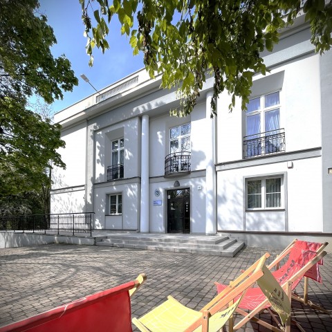 widok na wejście do budynku, przed nim kilka leżaków