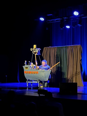występ sceniczny, teatr lalek, mężczyzna kuca za statkiem w dłoniach trzyma marionetki