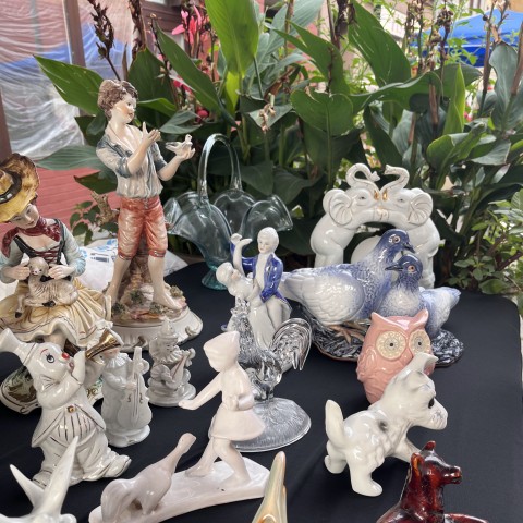 stoisko z figurkami z porcelany i szkliwa, w tle kwiat doniczkowy
