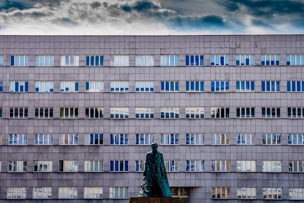 Fotografia przedstawia gmach budynku wydziału humanistycznego UŚ. Na pierwszym planie pomnik Wojciecha Korfantego. Autor: Moderna © Krzysztof Szlapa 2021