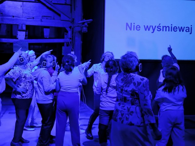 grupa osób tańczy, w tle na ekranie hasło: nie wyśmiewaj