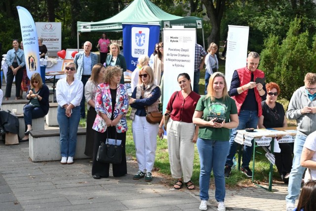 Plener, na placu, grupa osób stoi, w tle namiot i banery. 