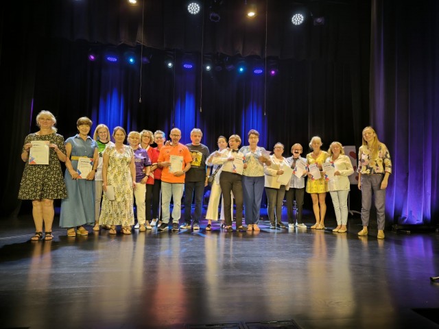 grupa osób na scenie pozuje do zdjęcia z dyplomami