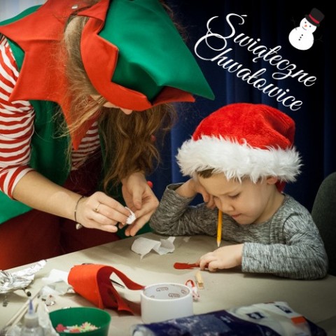 Przy stole siedzi dziecko z czapką Św. Mikołaja, a obok niego stoi kobieta w przebraniu